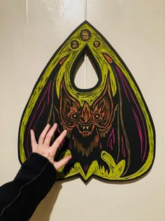 a hand reaching up to a bat shaped paper cutout on the side of a wall