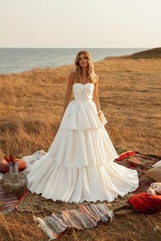 a woman in a white dress is standing on a blanket by the water and looking at her cell phone