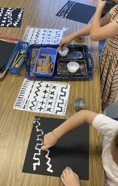 two children are making letters on paper at a table with scissors and other items in front of them