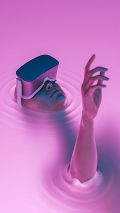 a pink and blue object floating in water next to a person's hand reaching for it