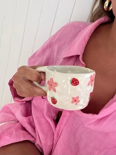 a woman in a pink dress holding a white cup with strawberries painted on it