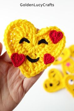 a hand holding a crocheted heart with emoticting hearts on the side