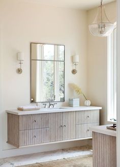 a white bathroom with two sinks and a large mirror above the sink is an elegant chandelier