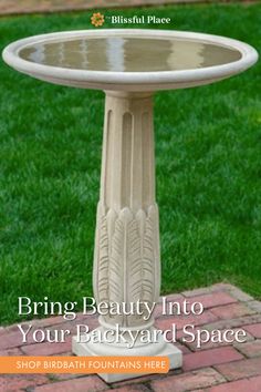 a white bird bath sitting on top of a brick floor next to grass and flowers