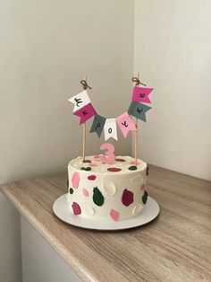 a birthday cake with pink, green and white decorations sitting on top of a wooden table