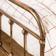 a metal bed frame with white and red bedspread on top of wooden flooring