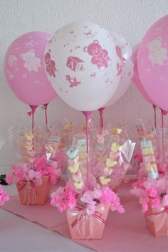 there are many balloons and candy in the vases on the pink table clothed