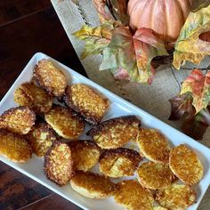 there are some fried food on a white plate next to pumpkins and autumn leaves