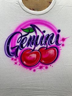 a white tank top with graffiti writing and cherries on the chest, in front of a window