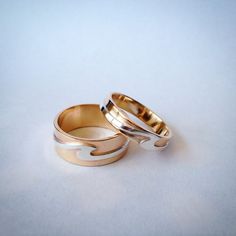 two gold wedding rings sitting next to each other on a white surface with one ring in the middle