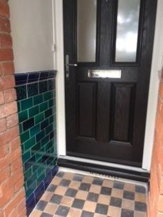 a black door is on the side of a brick wall and tiled floor in front of it