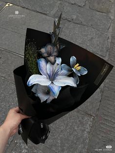 a hand holding a black paper bag with blue flowers on the top and one white flower in the middle