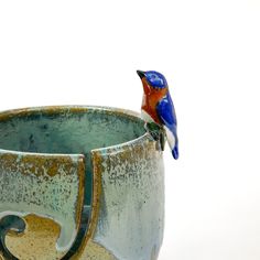 a blue and red bird sitting on top of a ceramic cup in the shape of a vase