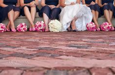 a bride and her bridal party sitting on a brick bench with their bouquets