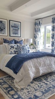 a large bed with blue and white comforter in a bedroom next to two windows