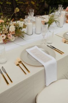 the table is set with white linens and gold place settings, candles, and flowers