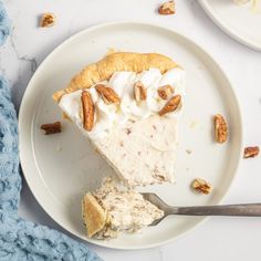 a piece of pie on a white plate with a fork next to it and pecans in the background