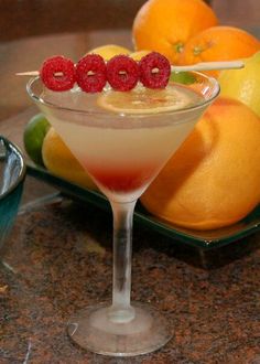 a martini with raspberries in it on a plate next to lemons and oranges