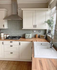 a kitchen with white cabinets and wood counter tops, an oven hood over the sink