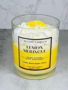 a yellow and white candle sitting on top of a marble counter next to a bottle of lemon meringue