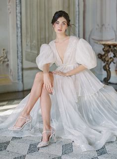 a woman sitting on the ground wearing high heels and a white dress with ruffles