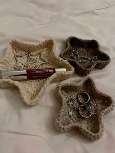 three small crocheted baskets with rings and lipstick in them sitting on a bed