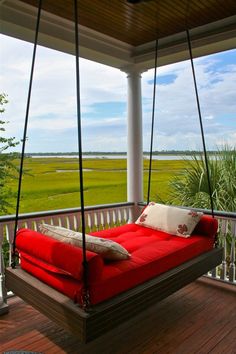 a red swing bed on a porch with a view of the marsh and grass in the background