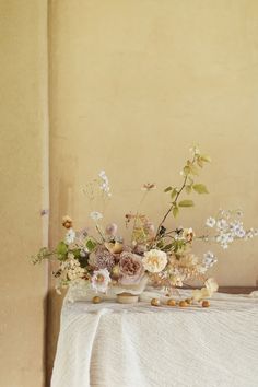 an arrangement of flowers on a table with a white linen draped over the tablecloth