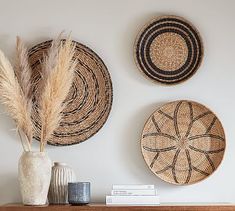 three woven baskets are hanging on the wall above a wooden mantel with two vases