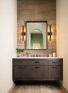 a bathroom vanity with two sinks and a large mirror above it, in front of a wood paneled wall