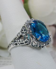 "Simulated Swiss Blue Topaz Ring Description Beauty Design#229 MADE TO ORDER This is a brand new stunning Art Nouveau/Victorian reproduction sterling silver filigree ring. The flawless oval-cut high-quality 4ct simulated Swiss blue topaz is 12mm by 10mm (just shy of 3/8\" inch) in dimension... The ring is 5/8th of an inch (16.5mm) NS (long) on the finger. The ring and gem sit 7mm off the finger. The inside of the band is marked 925 for sterling. Notice the beautiful filigree swirl like the craft Large Gemstone Rings, Oval Blue Topaz Ring As Gift, Handmade Blue Topaz Ring For Formal Occasions, Handmade Unique Blue Topaz Ring, Oval Blue Topaz Ring With Intricate Design, Blue Oval Topaz Ring With Intricate Design, Unique Handmade Blue Topaz Ring, Blue Topaz Ring With Intricate Design As Gift, Unique Blue Oval Topaz Ring