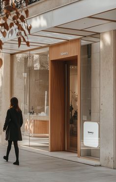 a woman walking down the sidewalk in front of a building with glass doors and windows