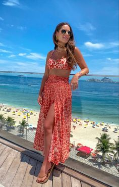 a woman standing on top of a wooden deck next to the ocean wearing a red and white dress