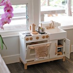 a toy kitchen set in front of a window with pink flowers on the windowsill