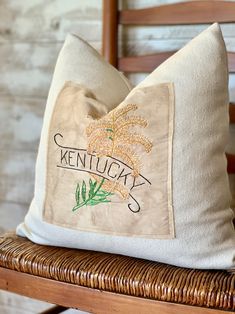 a decorative pillow with the name kentucky on it sitting on a wicker chair in front of a brick wall