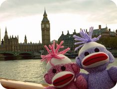 two stuffed animals sitting next to each other in front of a body of water with big ben in the background