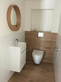 a white toilet sitting in a bathroom next to a wooden sink vanity and round mirror