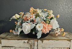 an arrangement of flowers in a black bowl on top of a wooden dresser against a gray wall