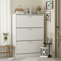 a white cabinet with three drawers in a living room next to a chair and potted plant