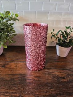 a pink glitter cup sitting on top of a wooden table next to potted plants