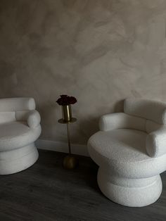 two white chairs sitting next to each other in front of a vase with a flower on it