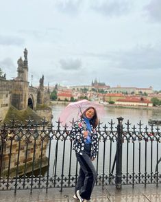 a woman holding an umbrella while standing next to a fence and looking at the camera