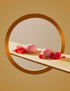 two desserts with pink icing and rose petals are on a wooden table in front of a circular frame