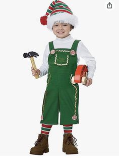 a little boy dressed in green overalls and a santa hat holding a hammer with both hands