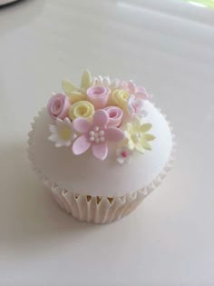 a white cupcake with pink and yellow flowers on it sitting on a counter top