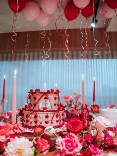 a table topped with a cake and lots of pink flowers next to red balloon garlands