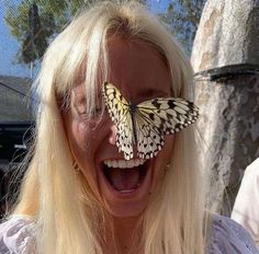 a woman laughing with a butterfly on her eye and mouth, in front of a tree