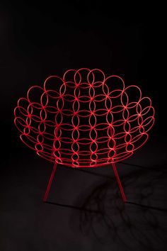 a red wire sculpture with circles on it's sides in the dark, against a black background