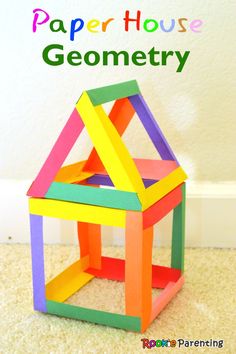 a toy house made out of colored construction paper on the floor in front of a white wall