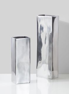 two silver vases sitting next to each other on a white counter top, one is empty